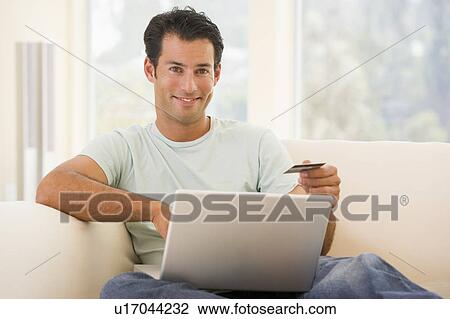 Man in living room using laptop and holding credit card smiling View Large Photo Image Stock Image - Man in living room using laptop and holding credit card smiling. Fotosearch