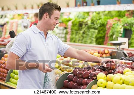 Stock Image - Man shopping for apples at a grocery store. Fotosearch