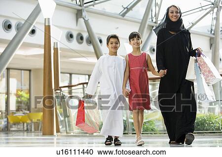 Stock Image - Woman and two young children walking in mall smiling (selective focus). Fotosearch