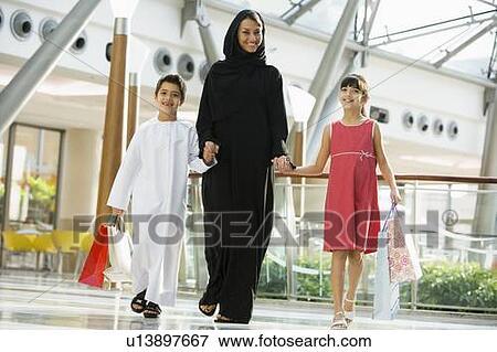 Stock Photo - Woman and two young children walking in mall smiling (selective focus). Fotosearch