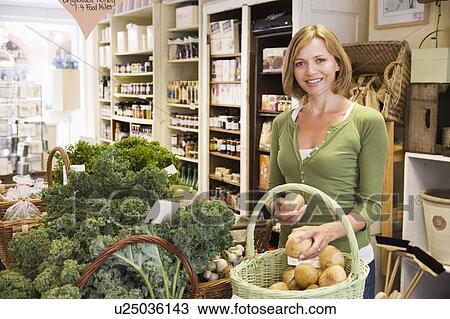 Stock Image - Woman in market looking at potatoes smiling. Fotosearch