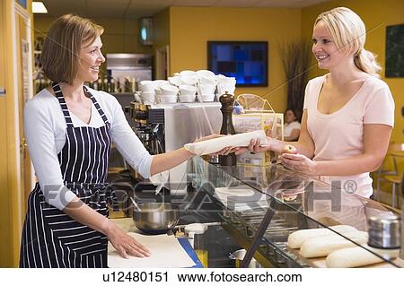 Stock Image - Woman standing at counter in restaurant serving customer and smiling. Fotosearch