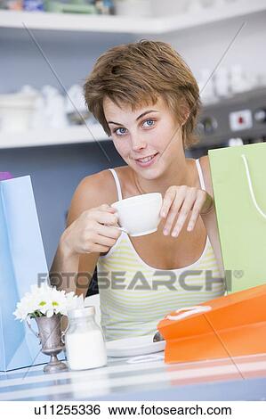 Young woman sitting at a table taking a break from shopping and drinking tea View Large Photo Image Stock Photograph - Young woman sitting at a table taking a break from shopping and drinking tea. Fotosearch