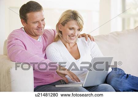 Couple in living room using laptop and smiling View Large Photo Image Stock Image - Couple in living room using laptop and smiling. Fotosearch