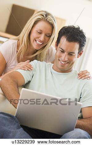 Couple in living room using laptop smiling View Large Photo Image Stock Photo - Couple in living room using laptop smiling. Fotosearch