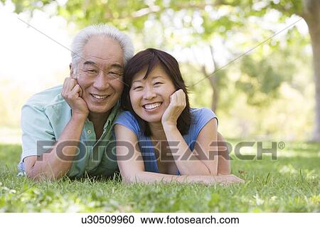 Stock Image - Couple relaxing outdoors in park smiling. Fotosearch