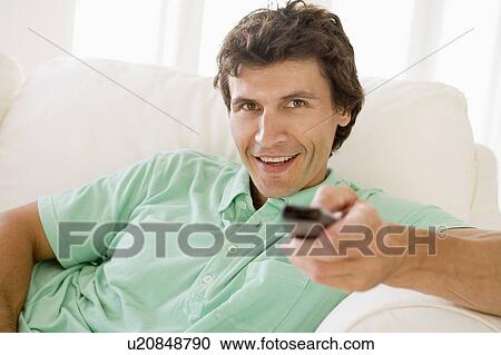 Man in living room holding remote control smiling View Large Photo Image Stock Image - Man in living room holding remote control smiling. Fotosearch