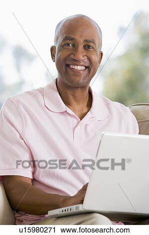 Man in living room using laptop and smiling View Large Photo Image Stock Image - Man in living room using laptop and smiling. Fotosearch