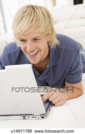 Stock Photograph - Man in living room with laptop smiling. Fotosearch