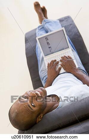 Man sitting in chair using laptop smiling View Large Photo Image Stock Image - Man sitting in chair using laptop smiling. Fotosearch