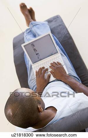 Man sitting in chair using laptop View Large Photo Image Stock Image - Man sitting in chair using laptop. Fotosearch