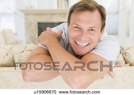 Stock Image - Man sitting in living room smiling. Fotosearch