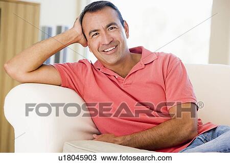 Stock Image - Man sitting in living room smiling. Fotosearch