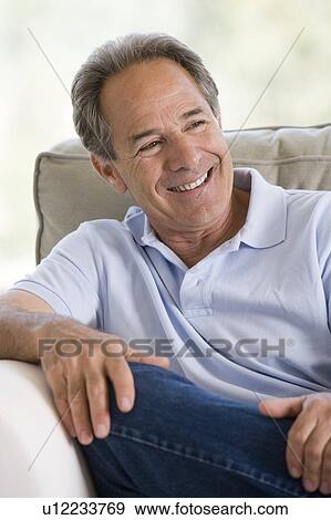 Man sitting in living room smiling View Large Photo Image Stock Photo - Man sitting in living room smiling. Fotosearch