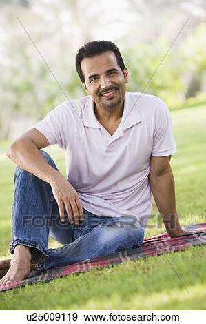 Stock Photo - Man sitting outdoors at park smiling (selective focus). Fotosearch