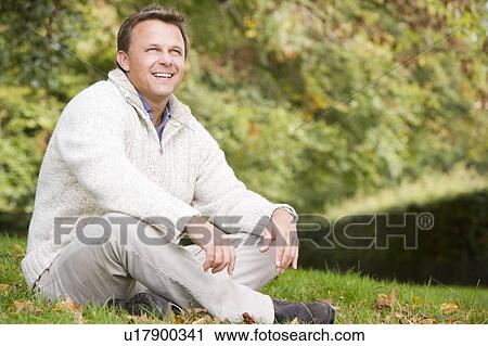 Stock Image - Man sitting outdoors smiling (selective focus). Fotosearch