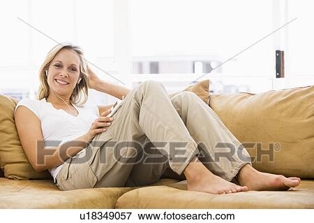 Stock Photo - Woman in living room listening to MP3 player smiling. Fotosearch