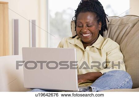 Woman in living room using laptop and smiling View Large Photo Image Stock Photograph - Woman in living room using laptop and smiling. Fotosearch