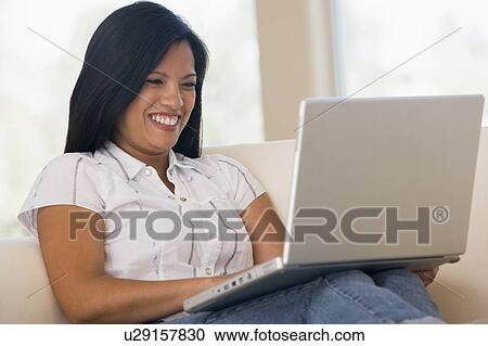 Stock Image - Woman in living room using laptop smiling. Fotosearch