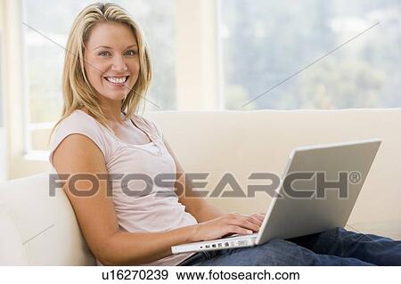 Stock Photo - Woman in living room using laptop smiling. Fotosearch