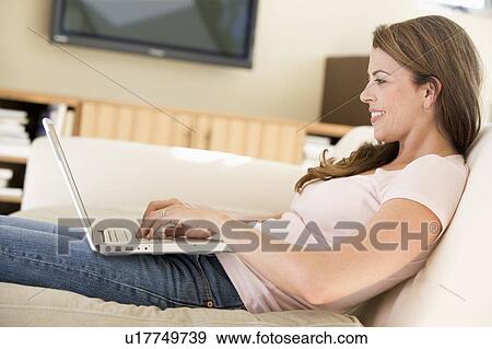Stock Photo - Woman in living room using laptop smiling. Fotosearch