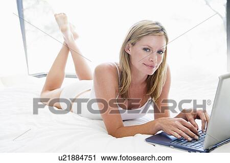 Woman lying in bed with laptop smiling View Large Photo Image Stock Image - Woman lying in bed with laptop smiling. Fotosearch