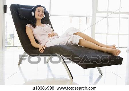 Stock Photo - Woman sitting in chair wearing headphones smiling. Fotosearch