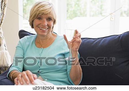 Picture - Woman sitting in living room with drink smiling. Fotosearch