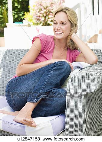 Stock Photo - Woman sitting outdoors on patio smiling. Fotosearch
