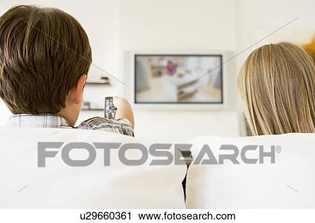 Stock Image - Young boy and young girl in living room with remote control and flat screen television. Fotosearch