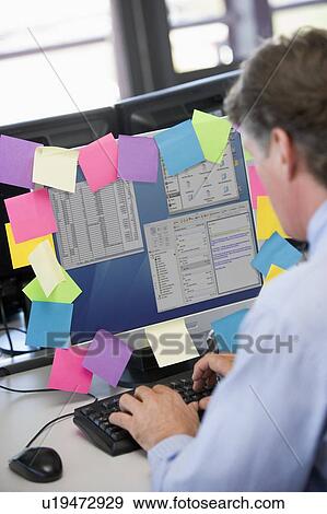 Businessman in office typing at computer with notes on it View Large Photo Image Stock Photo - Businessman in office typing at computer with notes on it. Fotosearch
