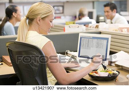 Businesswoman in cubicle using laptop and eating salad View Large Photo Image Stock Photo - Businesswoman in cubicle using laptop and eating salad. Fotosearch