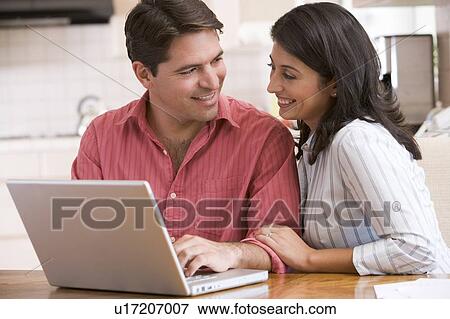 Couple in kitchen using laptop and smiling View Large Photo Image Stock Photo - Couple in kitchen using laptop and smiling. Fotosearch