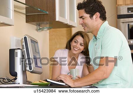 Picture - Couple in kitchen with computer and coffee smiling. Fotosearch