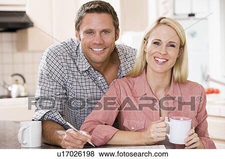 Couple in kitchen with newspaper and coffee smiling View Large Photo Image Stock Photo - Couple in kitchen with newspaper and coffee smiling. Fotosearch