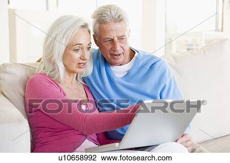 Stock Image - Couple in living room with laptop smiling. Fotosearch