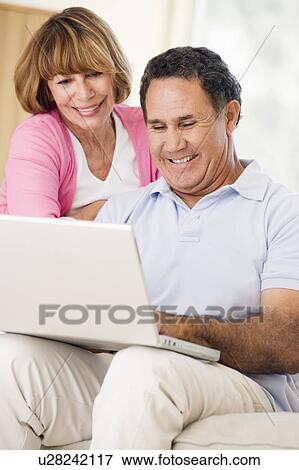 Stock Photo - Couple in living room with laptop smiling. Fotosearch