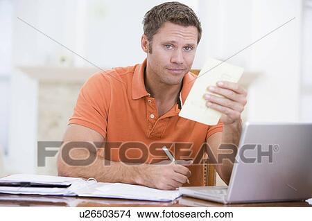 Man in dining room with laptop holding paperwork View Large Photo Image Picture - Man in dining room with laptop holding paperwork. Fotosearch