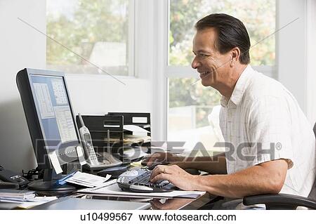 Stock Photo - Man in home office at computer smiling. Fotosearch