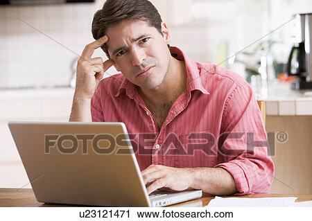 Man in kitchen using laptop frowning View Large Photo Image Stock Image - Man in kitchen using laptop frowning. Fotosearch
