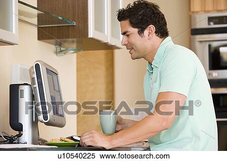 Stock Photography - Man in kitchen with coffee using computer and smiling. Fotosearch