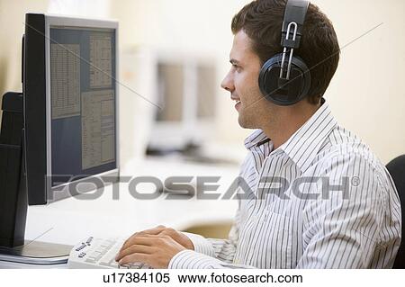 Man wearing headphones in computer room typing and smiling View Large Photo Image Stock Photography - Man wearing headphones in computer room typing and smiling. Fotosearch