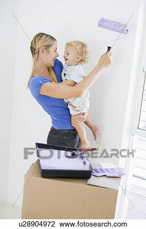 Mother holding son while painting room in new home smiling View Large Photo Image Stock Image - Mother holding son while painting room in new home smiling. Fotosearch