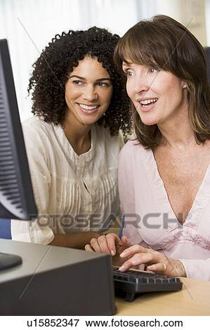 Stock Photo - Two women at a computer terminal typing (high key). Fotosearch