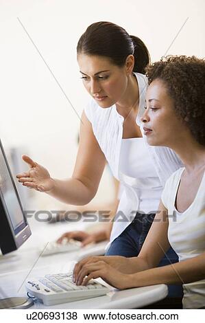 Stock Photo - Two women in computer room where one is assisting the other. Fotosearch