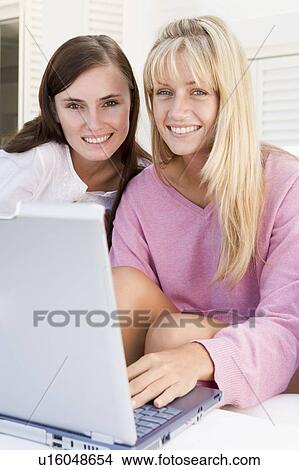 Picture - Two women on patio using laptop smiling. Fotosearch