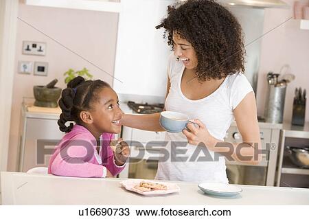 Stock Image - Woman and young girl in kitchen with cookies and coffee smiling. Fotosearch