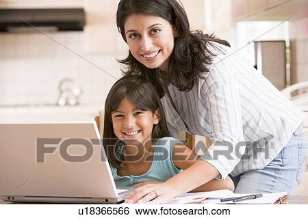 Stock Photograph - Woman and young girl in kitchen with laptop and paperwork smiling. Fotosearch