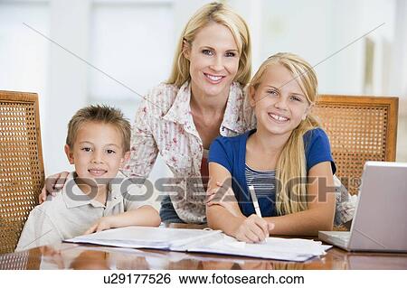 Woman helping two young children with laptop do homework in dining room View Large Photo Image Stock Photograph - Woman helping two young children with laptop do homework in dining room. Fotosearch