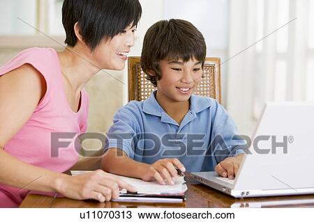 Woman helping young boy with laptop do homework in dining room smiling View Large Photo Image Stock Image - Woman helping young boy with laptop do homework in dining room smiling. Fotosearch